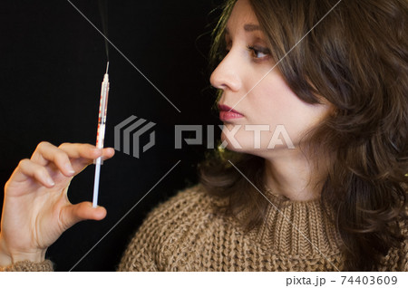 Vaccine concept. Female portrait of caucasian girl holding a syringe and looking at it on black background in studio. Vaccine concept. Female portrait of caucasian girl holding a syringe and looking at it on black background in studio. 74403609