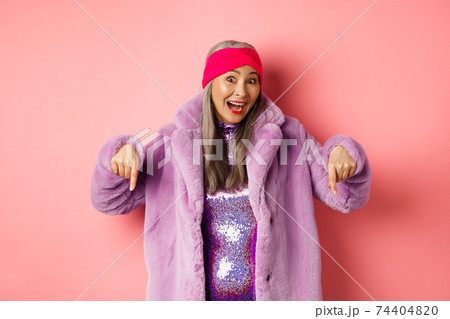 Fashion and shopping concept. Excited asian elderly woman checking out special deal, pointing fingers down and smiling happy at camera, showing advertisement, pink background Fashion and shopping concept. Excited asian elderly woman checking out special deal, pointing fingers down and smiling happy at camera, showing advertisement, pink background 74404820