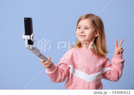 Little girl blogger influencer records videos from the blog on a smartphone, communicates with subscribers, puts likes, takes selfies,, remote learning on an isolated background. Little girl blogger influencer records videos from the blog on a smartphone, communicates with subscribers, puts likes, takes selfies,, remote learning on an isolated background. 74406422