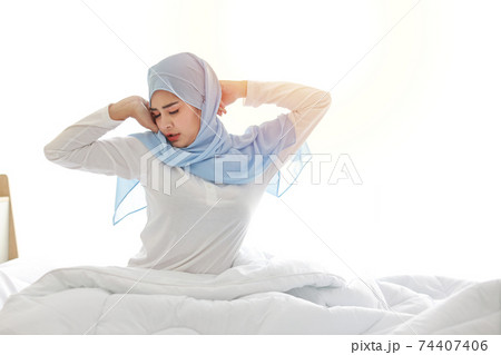 Beautiful asian muslim woman stretching her arms after getting up in the morning on bed at sunrise in bedroom. Cute young girl with blue hijab standing and relaxing with happy and smiling face. Beautiful asian muslim woman stretching her arms after getting up in the morning on bed at sunrise in bedroom. Cute young girl with blue hijab standing and relaxing with happy and smiling face. 74407406