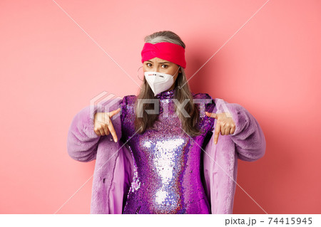 Coronavirus and shopping concept. Stylish asian elderly woman in purple clothes and face mask, pointing fingers down, showing promo, pink background Coronavirus and shopping concept. Stylish asian elderly woman in purple clothes and face mask, pointing fingers down, showing promo, pink background 74415945