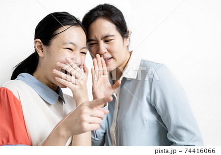 Asian woman gossiping slander in girl ear,aspersion, defamation,speak to scornful abuse,negative facial expression,female student pointing the finger with the hand covering the mouth laughing ridicule 74416066