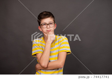 a boy with glasses looks thoughtfully into the distance on a dark gray background. 74417741