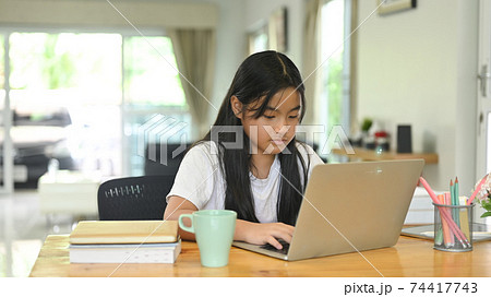 A school kid is doing her homework with a computer laptop at the wooden working desk. 74417743