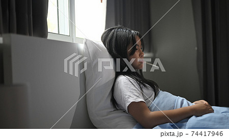 A little sick girl covered in a blanket is lying on the bed and measuring the temperature. 74417946