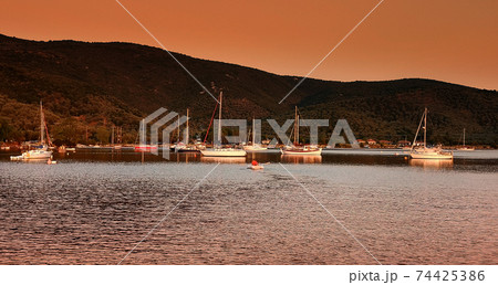 Sailboats anchored in a beautilful bay at sunset Sailboats anchored in a beautilful bay at sunset 74425386