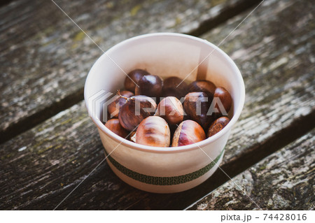 Fresh roasted chestnut portion in paper bowl on the rustic wooden table. Take away food. Selective focus. Fresh roasted chestnut portion in paper bowl on the rustic wooden table. Take away food. Selective focus. 74428016