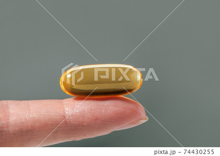 Female hand holding a big yellow capsule of nutritional supplement. Food supplement, vitamin D, omega, vitamin C. 74430255