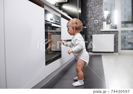 Infant baby boy near oven in home kitchen. Infant baby boy near oven in home kitchen. 74430597