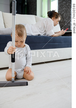 Baby boy play with mop, while mother surfing in your smartphone lying on couch Baby boy play with mop, while mother surfing in your smartphone lying on couch 74430599