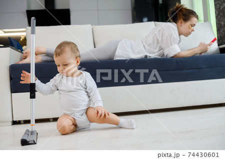 Baby boy play with mop, while mother surfing in your smartphone lying on couch Baby boy play with mop, while mother surfing in your smartphone lying on couch 74430601