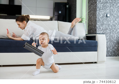 Baby boy play with mop, while mother surfing in your smartphone lying on couch 74430612