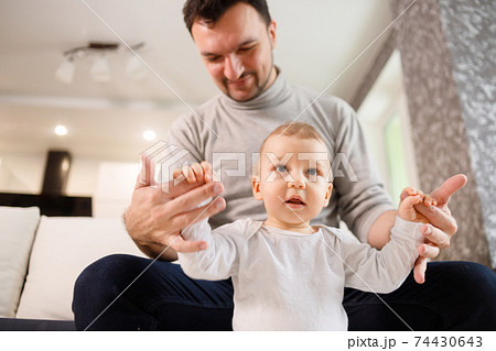 Young father assisting walking his infant son teaching to walk at home. Daddy helps son attempting to walk 74430643