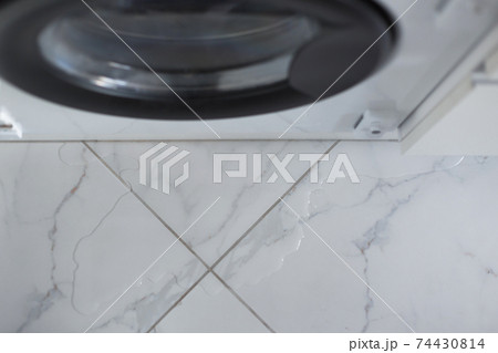 Spilled water leaked from washing machine built into the kitchen furniture. Spilled water on the tiled floor, flooding. Spilled water leaked from washing machine built into the kitchen furniture. Spilled water on the tiled floor, flooding. 74430814