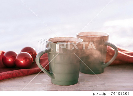 Vintage rustic card with green porcelain cups of tea on white wooden table decorated with red Christmas balls. Winter seasonal holiday background. 74435102