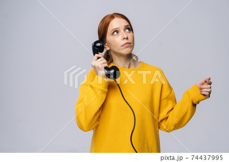 Dreamy young woman in stylish yellow sweater talking on retro phone and looking away 74437995