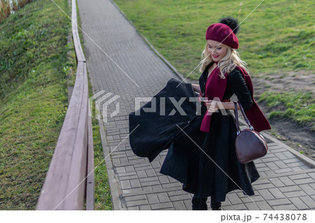 A cheerful girl walks up the stairs in a burgundy palette and biret, with a charismatic appearance in black clothes, in the fall against the background of trees there is a blue sky. A cheerful girl walks up the stairs in a burgundy palette and biret, with a charismatic appearance in black clothes, in the fall against the background of trees there is a blue sky. 74438078