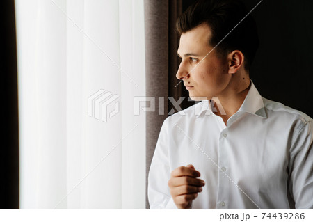 young man in a white shirt fastens cufflinks on sleeves near the window young man in a white shirt fastens cufflinks on sleeves near the window 74439286