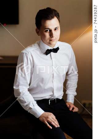 young man in white shirt and bow tie sitting in chair. business portrait 74439287