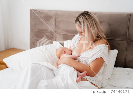 woman is sitting with a newborn in a white bed feeding breast milk. woman is sitting with a newborn in a white bed feeding breast milk. 74440172