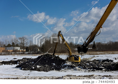 Heavy construction equipment during excavation at construction in the excavator working on earthmoving at pit on winter backhoe digs Heavy construction equipment during excavation at construction in the excavator working on earthmoving at pit on winter backhoe digs 74440493