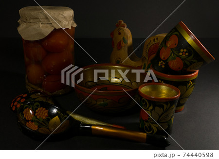 Glass jar of preserved tomato, a spoon with folk painting and a wooden bowl 74440598