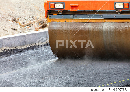 The metal cylinder of the large vibratory road roller compacts the fresh asphalt, dampening the hot surface. The metal cylinder of the large vibratory road roller compacts the fresh asphalt, dampening the hot surface. 74440738
