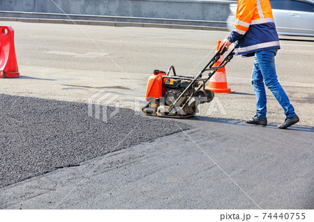 A road worker compacts asphalt with a petrol vibratory plate compactor. 74440755