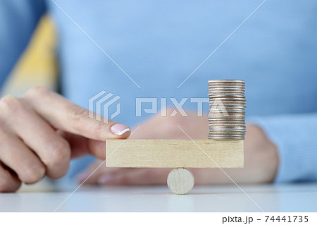 Tower of coins on wooden block and finger on other side 74441735