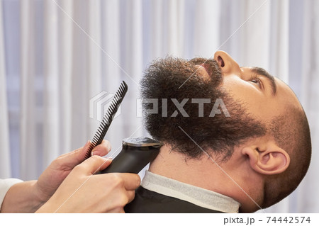 Hand of barber trimming beard. 74442574