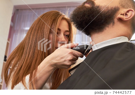 Female barber is grooming beard. 74442577