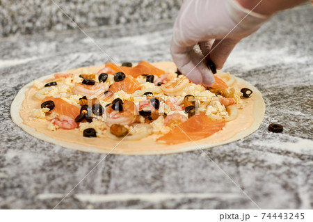 Adding black olives to pizza. 74443245