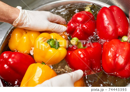 Hands in gloves washing peppers into bowl, close up. 74443393