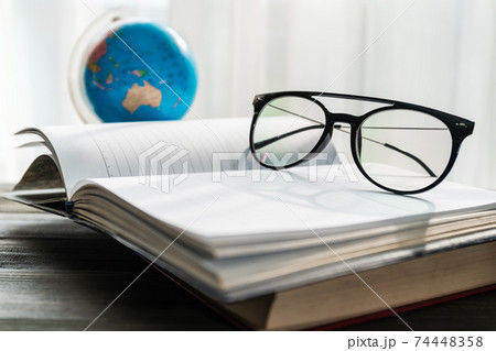 Reading glasses put on open book beside the window 74448358