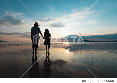 Silhouette of asian mother and daughter holding hand and walking on the beach together at the sunset time with beautiful sea and sky. Family enjoy with nature concept. Silhouette of asian mother and daughter holding hand and walking on the beach together at the sunset time with beautiful sea and sky. Family enjoy with nature concept. 74448866