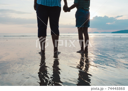Silhouette of asian mother and daughter holding hand together standing on the beach looking at the beautiful sea and sky at the sunset time. Silhouette of asian mother and daughter holding hand together standing on the beach looking at the beautiful sea and sky at the sunset time. 74448868