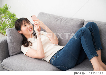 ソファーに寝転がってスマホを操作する女性 74451514