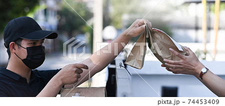 Close up view of customer receiving paper bag with food from delivery people at house door. Close up view of customer receiving paper bag with food from delivery people at house door. 74453409