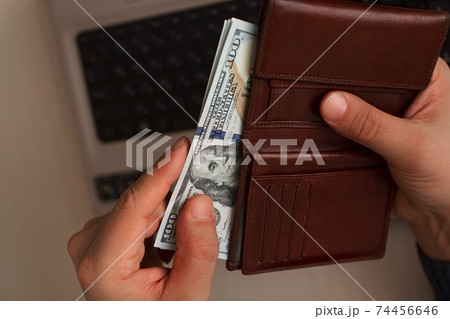 one hundred dollar banknotes in bundle protruded from leather brown wallet in men's hand on laptop background one hundred dollar banknotes in bundle protruded from leather brown wallet in men's hand on laptop background 74456646