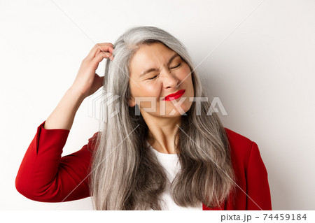 Close up of senior asian woman scratching head and looking bothered by itching, standing over white background 74459184
