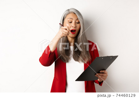 Successful asian female entrepreneur taking notes on clipboard, working on report and looking excited, standing over white background 74460129