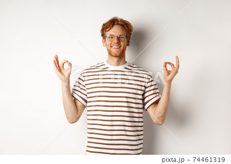 Cheerful redhead man in glasses have all under control, showing okay signs and smiling satisfied, standing relaxed over white background Cheerful redhead man in glasses have all under control, showing okay signs and smiling satisfied, standing relaxed over white background 74461319