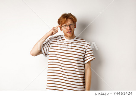 Annoyed young man with red hair scolding person for being stupid, pointing at head and staring at camera, white background Annoyed young man with red hair scolding person for being stupid, pointing at head and staring at camera, white background 74461424