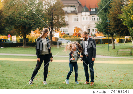 A happy family of three runs through the grass in Austria's old town.A family walks through a small town in Austria.Europe.Velden am werten Zee 74463145