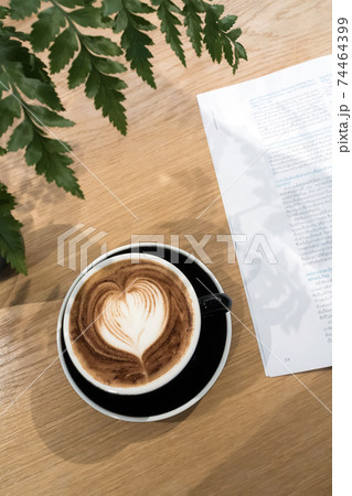 Coffee cup and a part of book on wood table with ornament fern leaf. 74464399
