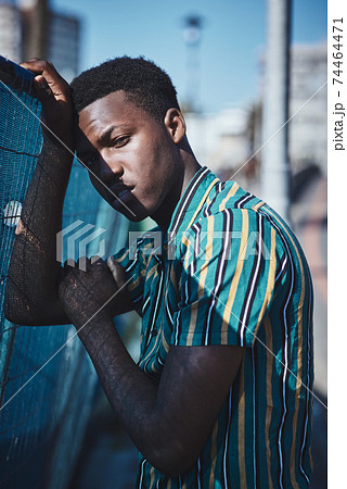 A portrait of a young African man leaning against a fence. A portrait of a young African man leaning against a fence. 74464471