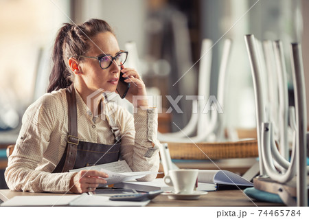 Restaurant owner consults bookeeping with her accountant sitting over paperwork with a coffee Restaurant owner consults bookeeping with her accountant sitting over paperwork with a coffee 74465784