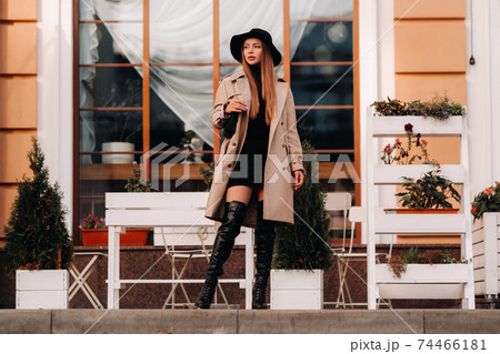 Stylish young woman in a beige coat in a black hat on a city street. Women's street fashion. Autumn clothing.Urban style 74466181