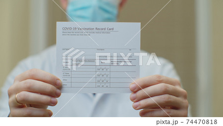 Doctor is holding a vaccination record card and corona virus vaccine vials. Passport of immunity to the coronavirus in the hands of a male doctor. Health passport as proof of recovery from COVID-19. Doctor is holding a vaccination record card and corona virus vaccine vials. Passport of immunity to the coronavirus in the hands of a male doctor. Health passport as proof of recovery from COVID-19. 74470818
