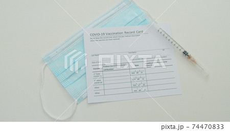 Medical mask and COVID-19 vaccine on vaccination record card approved by CDC with corona virus vaccine vials. White background. Medical mask and COVID-19 vaccine on vaccination record card approved by CDC with corona virus vaccine vials. White background. 74470833